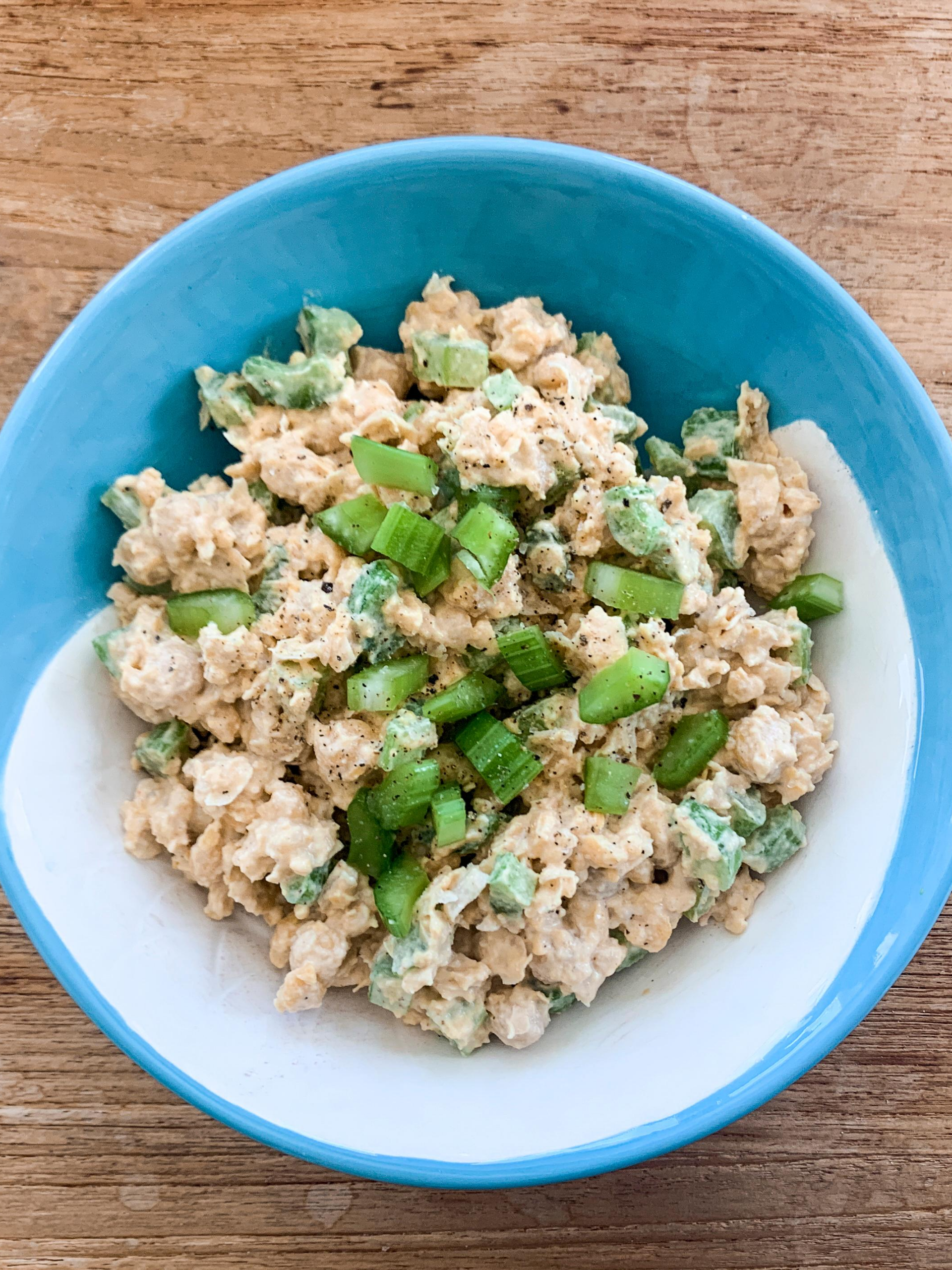 chickpea salad with celery in blue and white bowl on light wood background