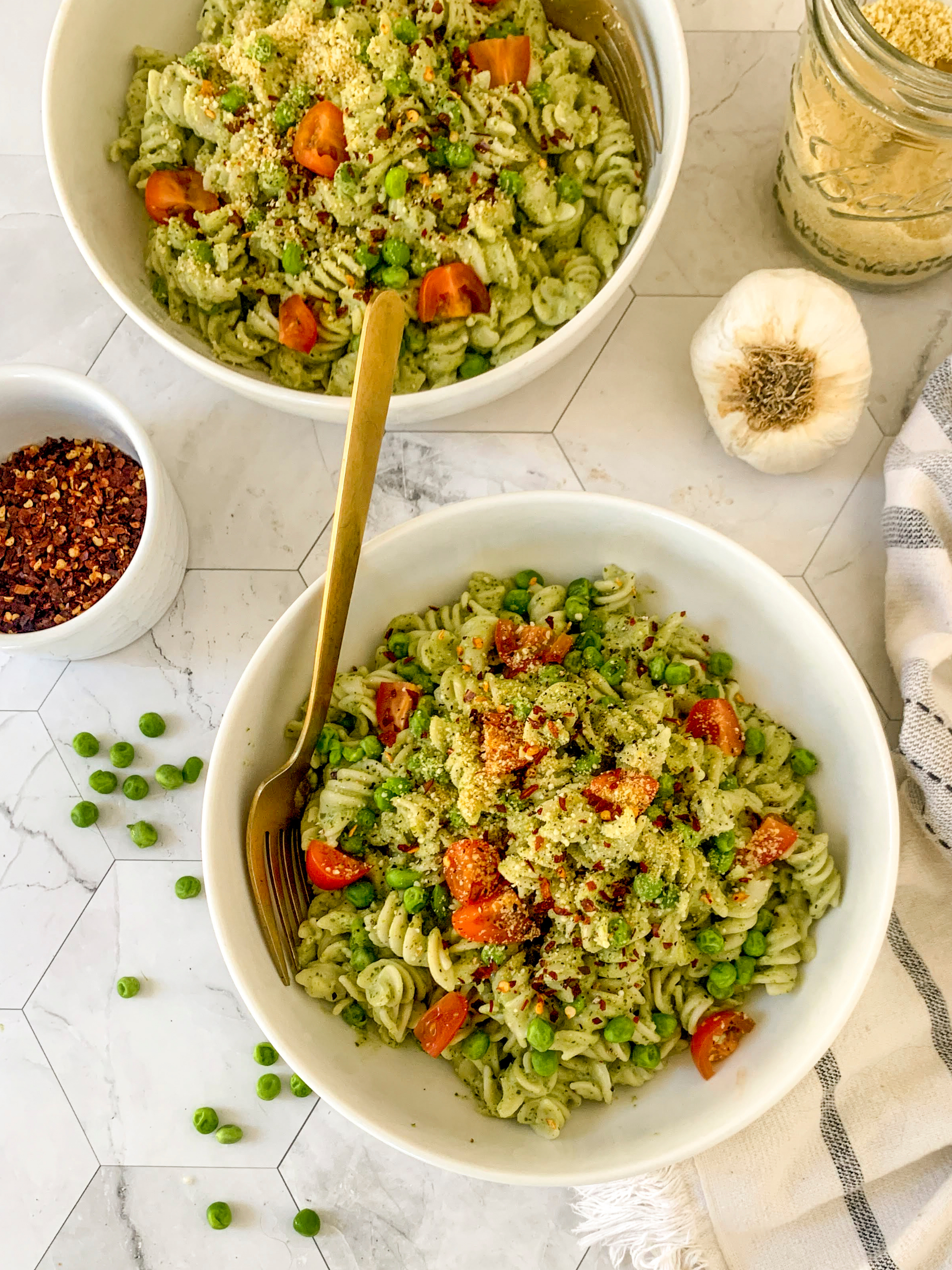 Pesto pasta served in bowls with peas and tomatoes